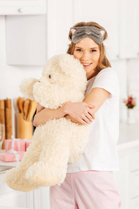 美丽的微笑女孩抱着泰迪熊，在家里的睡衣派对中看着相机