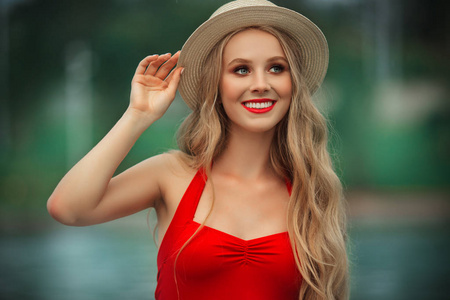 美丽的微笑的少女穿着红色泳衣和帽子休息在游泳池与蓝色的水。暑假
