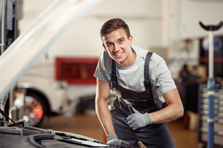 一个年轻人在工作时微笑着站在一辆汽车附近。汽车和车辆维修