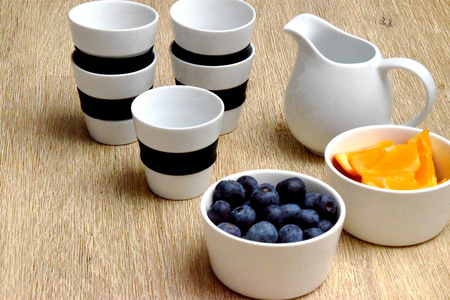 在木桌上的白色碗中加入牛奶罐和新鲜蓝莓和橙片
