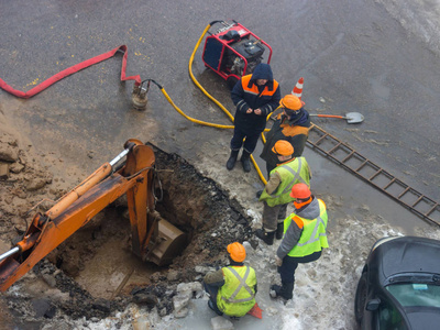 一群穿着反光背心的公共设施的道路工人正在讨论一个紧急情况，在在冬季中挖洞以消除管道泄漏