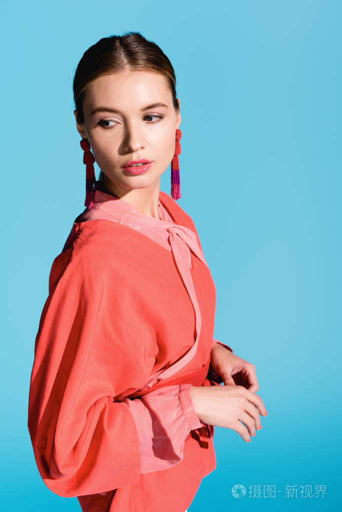 时尚的女孩摆着时髦的生活珊瑚服装,与蓝色隔离照片-正版商用图片18i