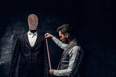 一位带着测量带的时装设计师在一个黑暗的裁缝工作室里检查一个定制的优雅男装的袖子长度