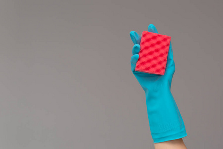 手中的橡胶手套持有彩色洗海绵在中性背景。 明泉弹簧清洗的概念。