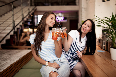两个漂亮的年轻微笑的女孩, 穿着休闲的衣服, 坐在一起, 在一个舒适的咖啡店看着镜头