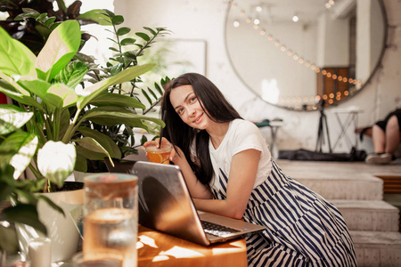 一个美丽的年轻苗条的女孩, 黑头发和眼镜, 穿着休闲的风格, 坐在桌旁, 在一个新的咖啡店与笔记本电脑