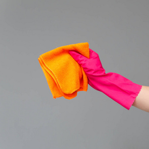 在中性背景下，用一只橡胶手套将一个明亮的微纤维粉尘夹在手中。春季清洁概念。