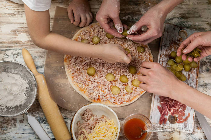 妈妈和她的孩子用手做美味的披萨配上火腿蔬菜和樱桃番茄近点