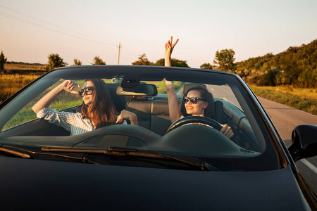 戴墨镜年轻女子驾驶敞篷车在阳光明媚的日子里, 两个戴着太阳镜的迷人