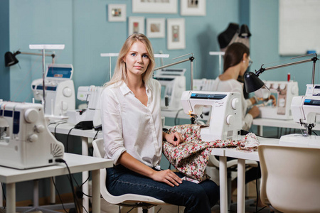 一个穿着白衬衫的漂亮金发碧眼的女人正在用电动缝纫机缝制。时尚裁缝师车间