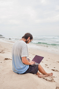 一个年轻人在海滩上的笔记本电脑工作。在海边海滩上工作的自由职业者