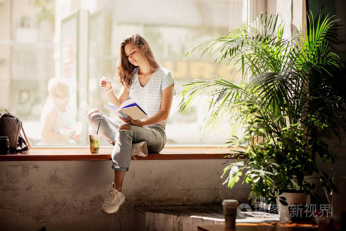 一个身材苗条,头发很长的年轻女孩, 穿着休闲装, 坐在窗台上, 在舒适