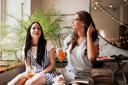 两个长着黑发的年轻美女, 穿着休闲的衣服, 坐在旁边, 在一家现代化的咖啡店里喝咖啡