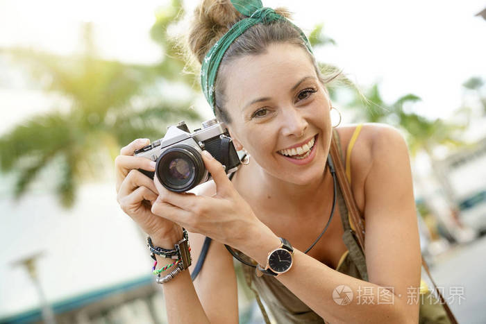 时尚年轻女性在城市环境中用老式相机拍照的肖像。