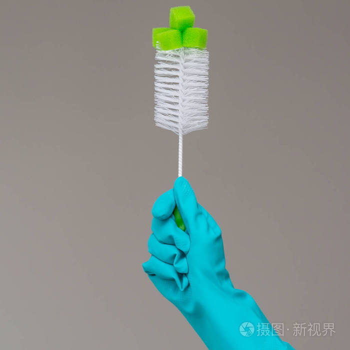 橡胶手套中的一只手将洗碗刷握在中性背景上明泉弹簧清洗的概念