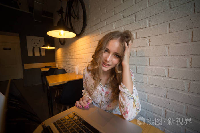 漂亮的年轻卷发冰雹女孩的照片与笔记本电脑微笑, 坐在咖啡馆