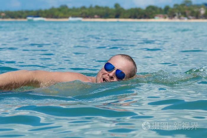 戴墨镜的男运动员在海里的水里游泳