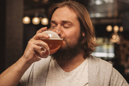 一个留着胡子的人闭上眼睛，在酒吧休息，一边喝着美味的手工啤酒。快乐轻松的男性顾客喝啤酒，在酒吧庆祝节日。啤酒节，放松概念