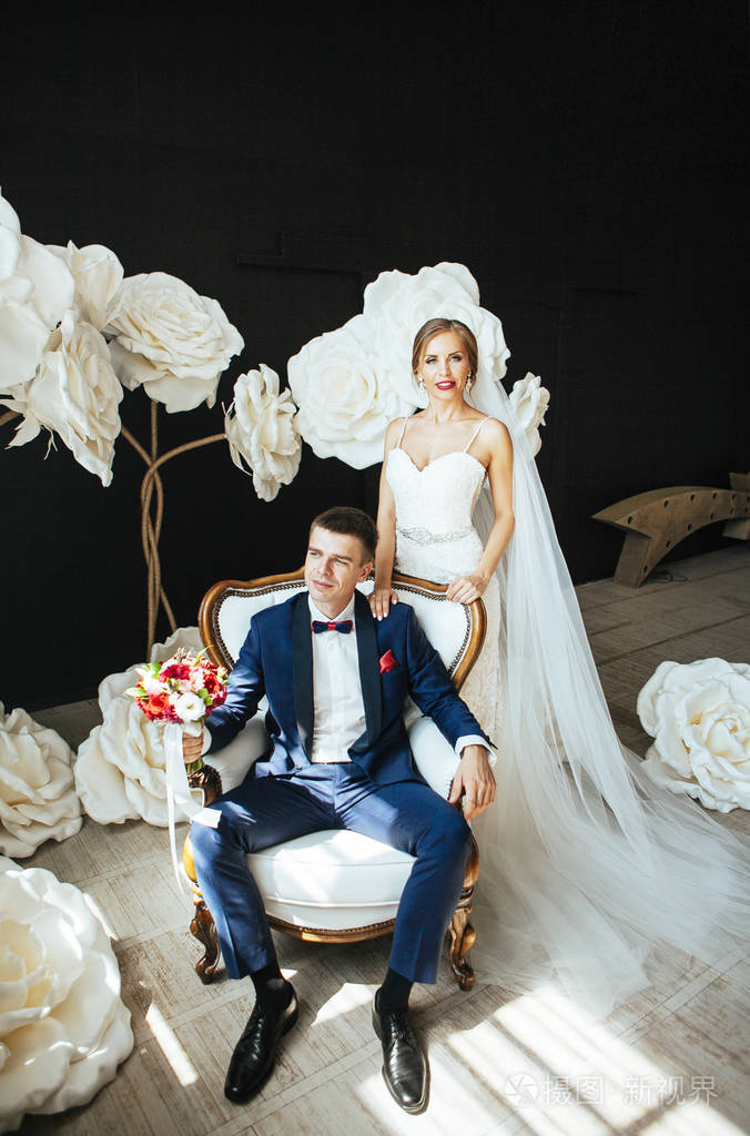 新娘轻轻地拥抱新郎的婚礼照片,在一个白色的巨大花朵的背景上.