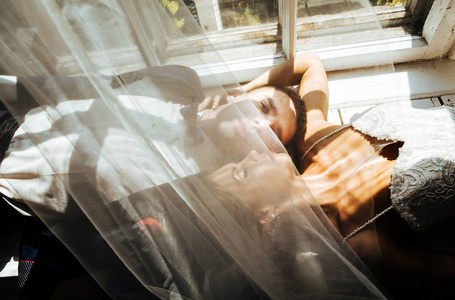 时尚的新娘和新郎在摄影棚举行的婚礼上，一对相爱的夫妇躺在窗户附近的地板上，照片是在一盏强光下拍摄的