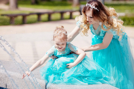 幸福快乐的家庭，母亲和她的小女儿在喷泉里玩飞溅。 公园里的户外。 新鲜的水。 晴天