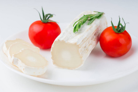 切好的羊奶酪，配上樱桃番茄和迷迭香叶，放在白色的桌子上，放在白色的陶瓷盘子上，正面观看