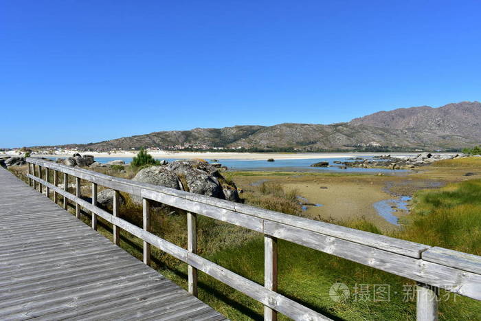 海滩有山湖和木板路。 岩石明亮的沙子和绿松石水。 晴天蓝天加利西亚西班牙。