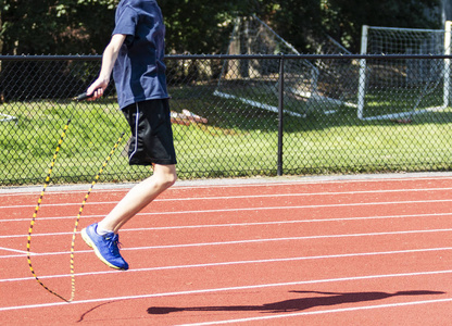 一名高中跑步者在夏末通过在跑道上跳绳进行交叉训练.照片
