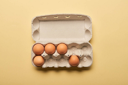 黄色背景纸板箱中棕色有机蛋的俯视图