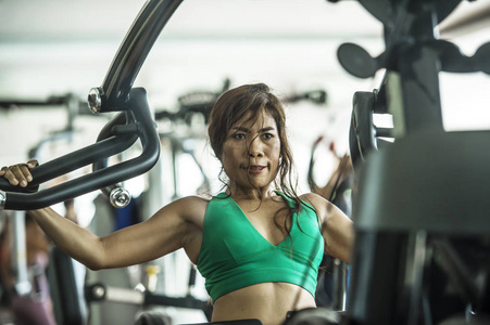 年轻的运动和坚定的亚洲印度尼西亚妇女努力工作的重量使用胸部健美健身机在健身俱乐部的决心和健康的生活方式概念