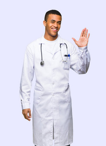 年轻的AFRO美国男医生用手在孤立的背景上愉快地表达着敬礼
