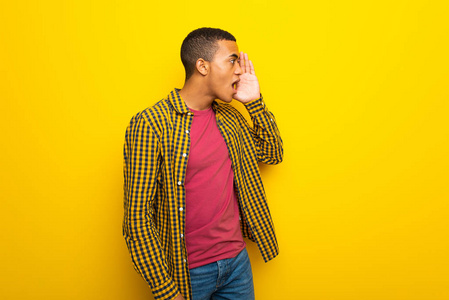 年轻的美国黑人男子在黄色背景上大声喊叫,嘴巴向侧面张开照片