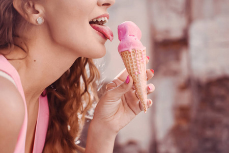特写一个年轻漂亮的女孩的肖像，卷发，穿着一件粉红色的连衣裙，拿着华夫饼冰淇淋喇叭舔和泡芙，微笑的生活方式
