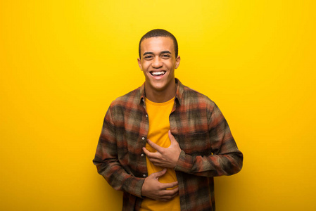 年轻的非裔美国男人，在充满活力的黄色背景上微笑，同时把手放在胸部