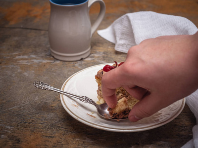 s hand takes a piece of homemade cake. In the background, a mug 