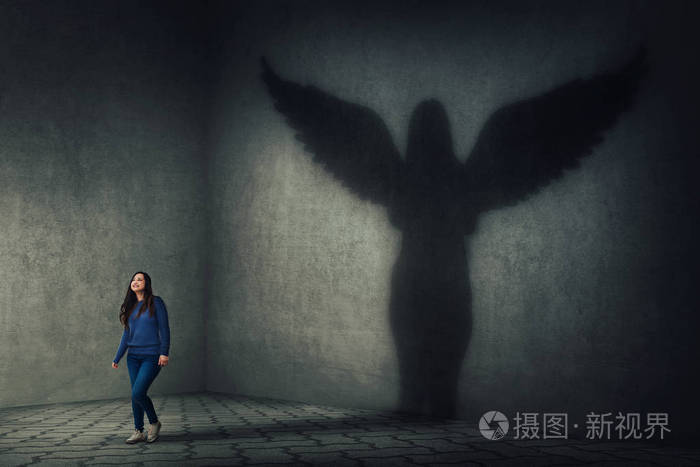 女子行走和铸造超级英雄的影子作为守护天使与翅膀在黑暗的房间墙上