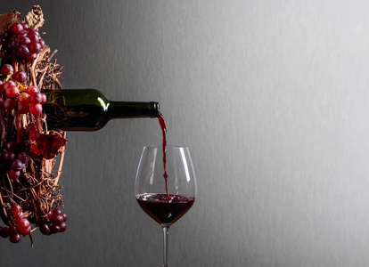 红酒从瓶子里倒进玻璃杯里. 带多汁葡萄的藤蔓花环.