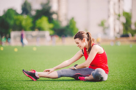 年轻美丽的白种人女人坐着做热身运动,热身肌肉,伸展绿草.