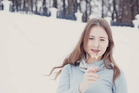 快乐和微笑的女孩在下雪时保持街道上的孟加拉灯。 冬季概念。 新年概念。