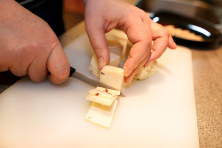 女人手切奶酪，她在厨房准备食物。 厨师在餐厅厨房桌子上的木板上用刀切奶酪。 家庭主妇用刀子把奶酪切成薄片。