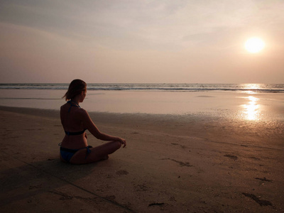 女孩坐在夕阳对面的沙滩上。