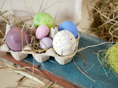 在包装中涂上多种颜色的鸡肉和鹌鹑蛋，复活节装饰干草，在浅色背景上，木板