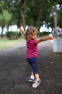 城市公园里穿条纹衬衫跳舞的卷发女孩的肖像。