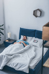 沮丧的男人躺在靠近相框的床上，家里抱着枕头上的女人的照片