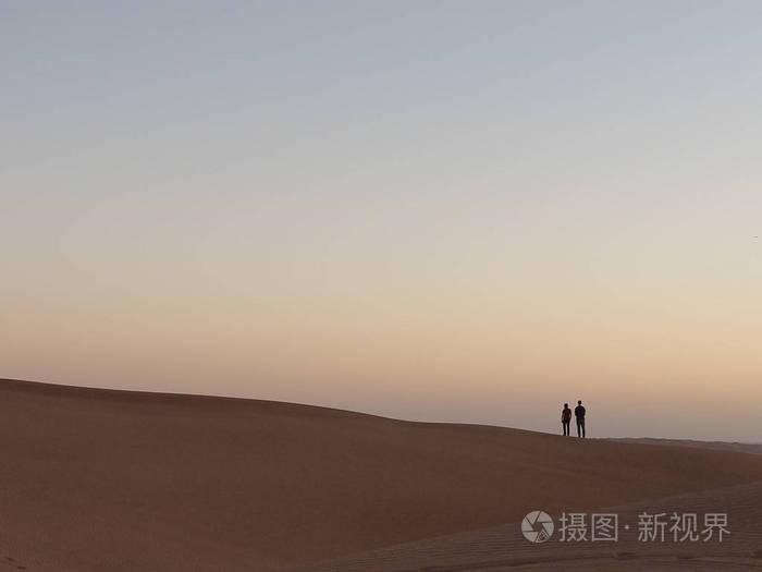 两个遥远的人站在沙丘在沙漠日落迪拜。