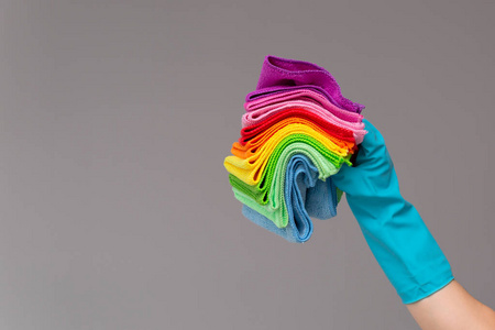 橡胶手套中的一只手将一套彩色微纤维布放在中性背景上。明春，清春的理念..