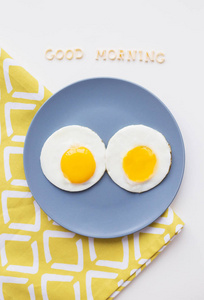 盘子里有两个鸡蛋和一张黄色餐巾，上面写着早上好