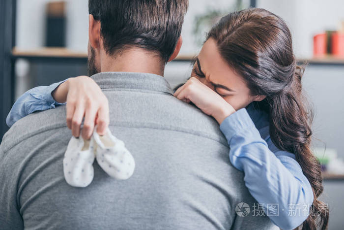 女人哭泣拥抱男人在家里抱着婴儿袜子悲伤的混乱概念