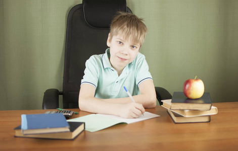 聪明的男孩坐在桌子旁，有许多书和红苹果。 教育概念。