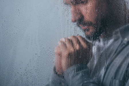 心烦意乱的人双手合十，透过雨滴和复印空间的窗户